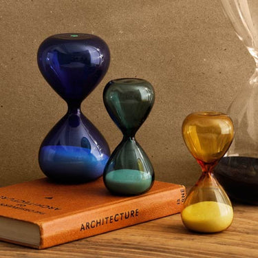 Three colored hourglasses on a book with a brown background