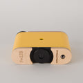 Yellow and black camera lens with 'F=173' and Racina branding on a gray background laying flat.