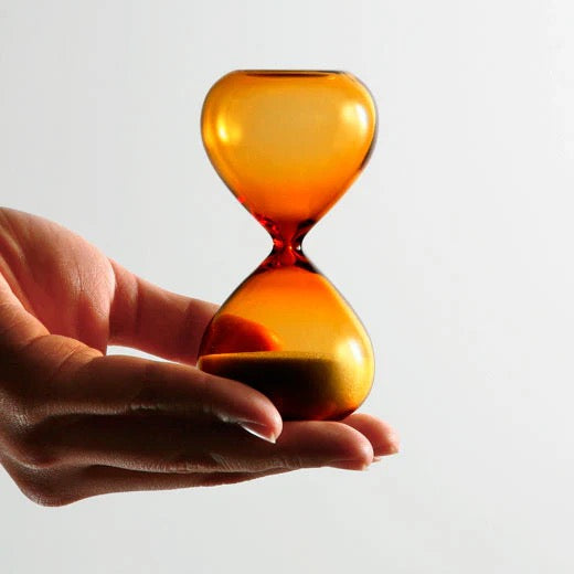 Hand holding a small 3 minute amber hourglass against a light gray background