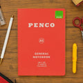 Red notebook with 'Penco' branding on a wooden surface with stationery items.