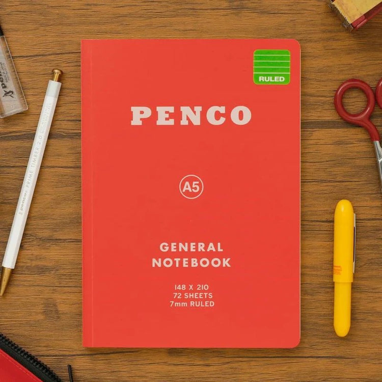 Red notebook with 'Penco' branding on a wooden surface with stationery items.